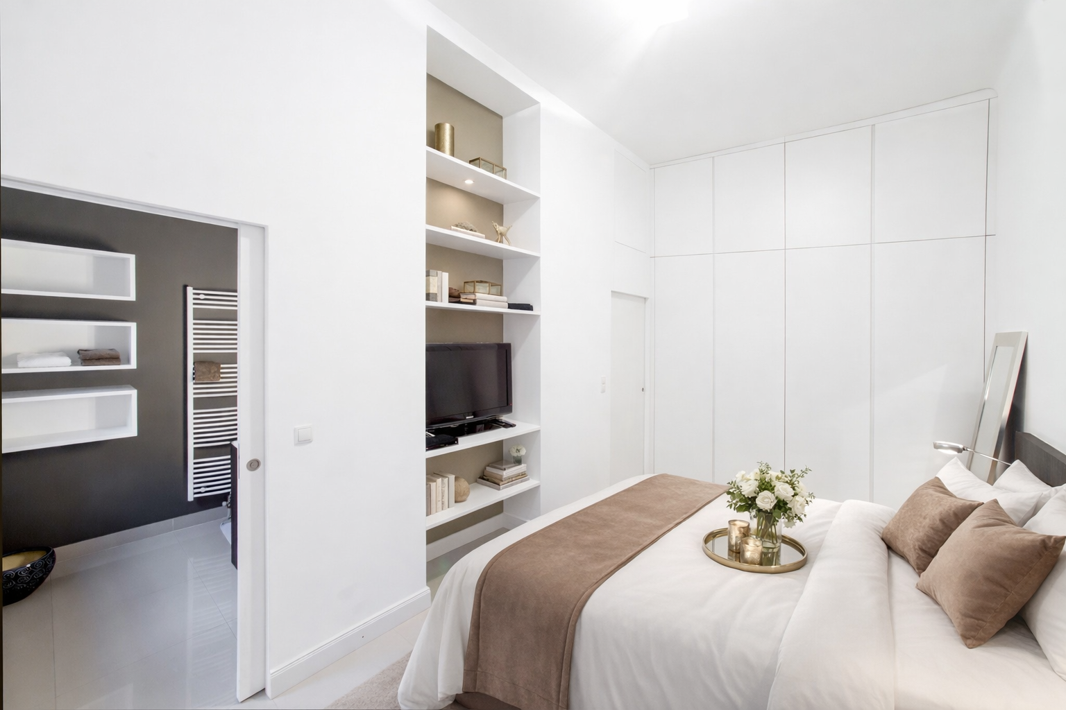 Serene white bedroom with double bed, built-in wardrobes and en-suite beyond
